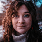 Woman with curly hair wearing a turtleneck and earrings outdoors at twilight.